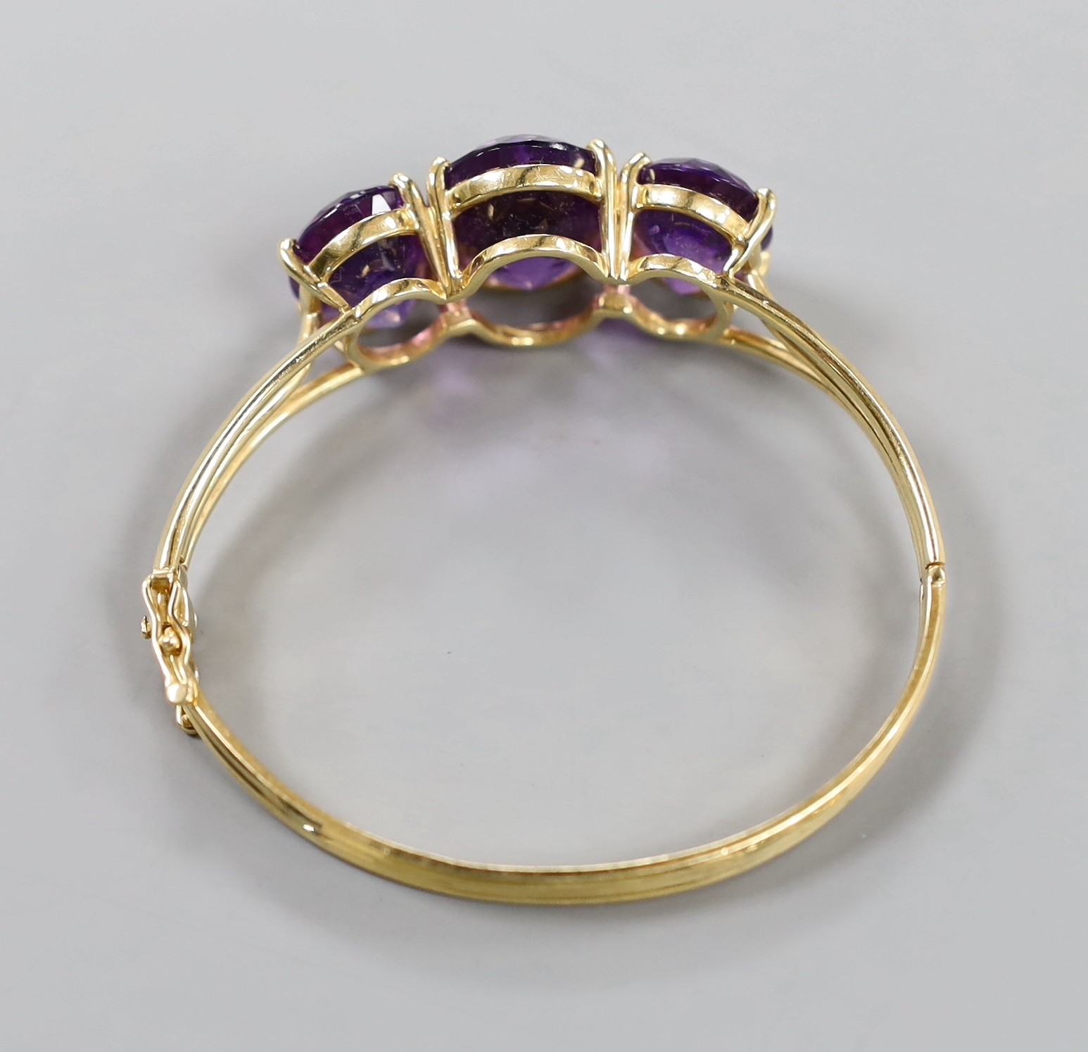 A modern 14k and three stone oval cut amethyst set hinged bangle, interior diameter 54mm, gross weight 24.8 grams.